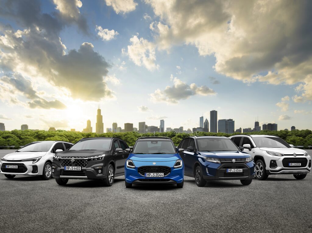 Fünf verschiedene Fahrzeugmodelle der Marke Suzuki in einer Reihe vor einer Stadt mit Wolkenhimmel. Durch klicken auf das Bild gelangt man zur Seite "Suzuki Tageszulassung".
